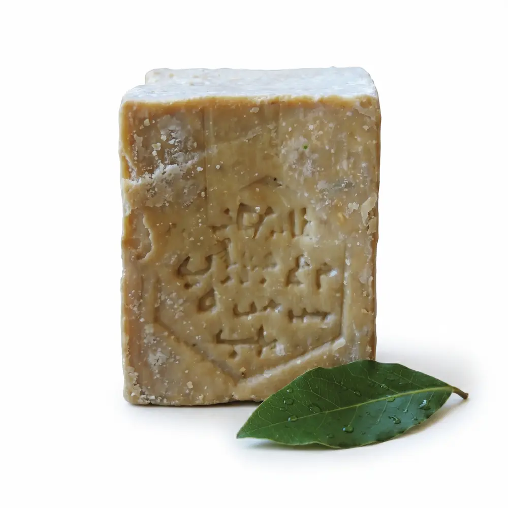 Primer plano frontal de una pastilla de Jabón de Alepo auténtico con sello de origen sirio sobre fondo neutro.